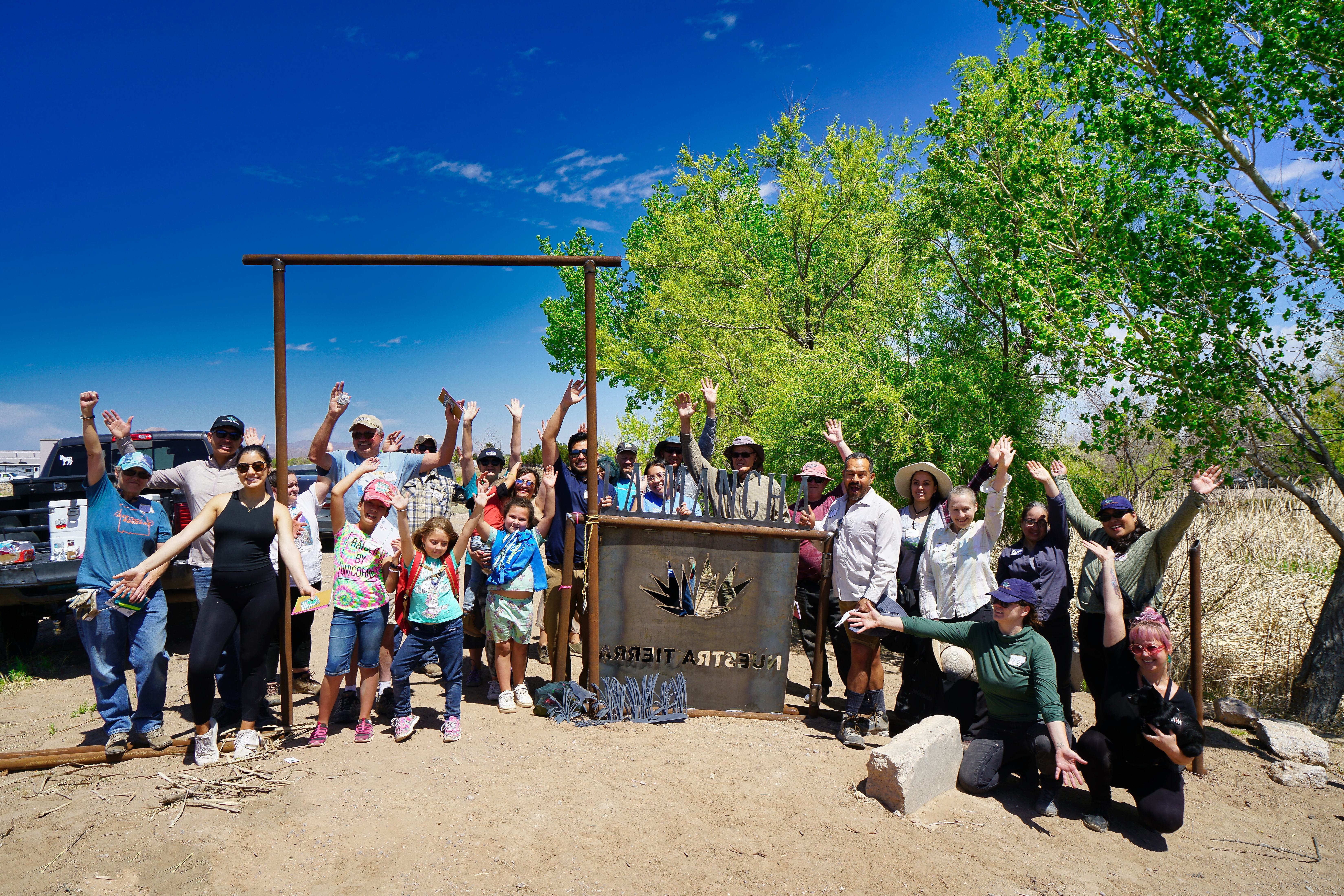 A large group of people pose outdoors in front of a sign